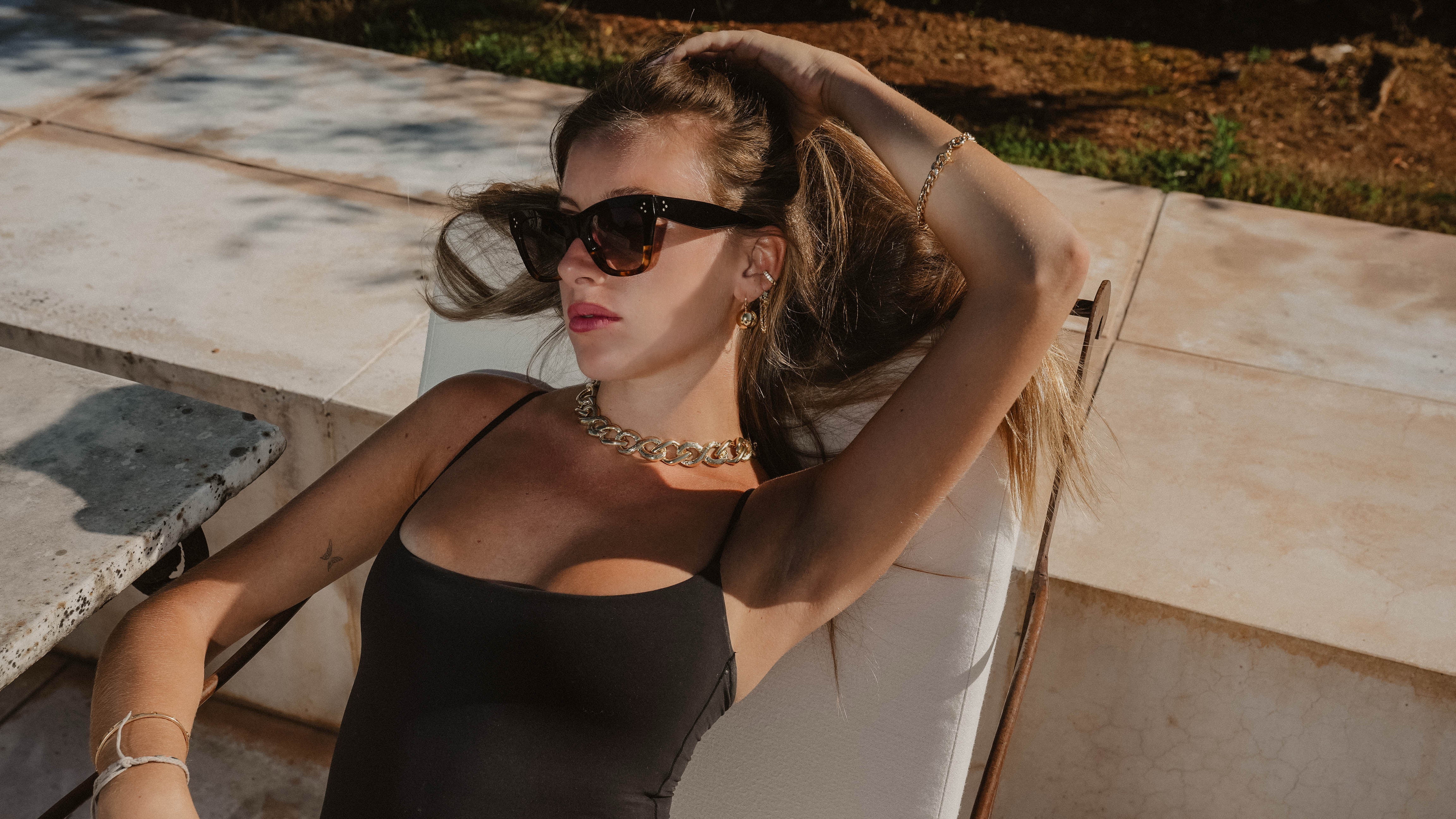 Woman sitting outdoors wearing sunglasses and a black top.
