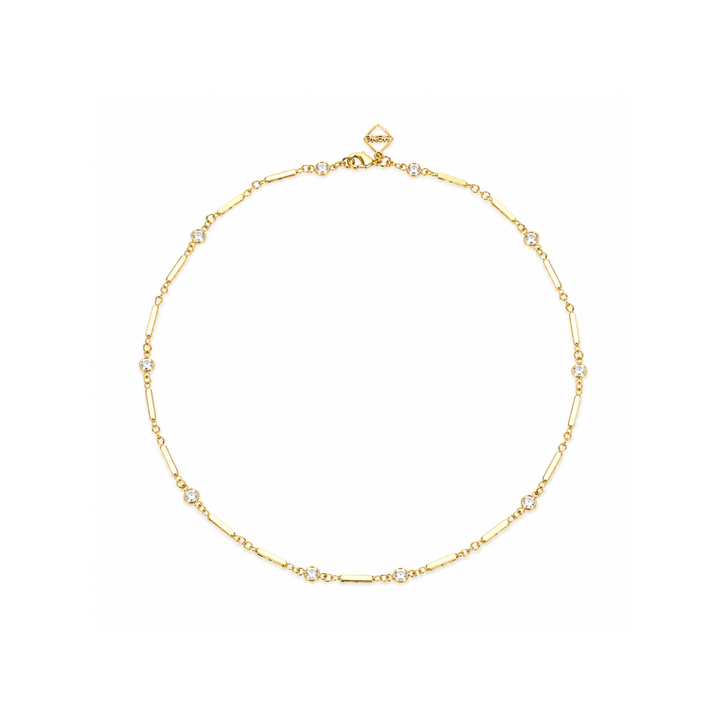 A delicate gold chain necklace with small clear gemstone accents, displayed in a circular shape against a solid white background.