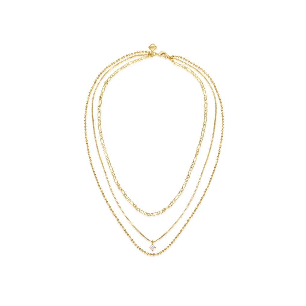 A delicate gold multi-strand necklace featuring three layered chains of varying textures, including a small clear crystal pendant, displayed on a clean white background.