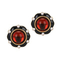 Pair of earrings with red gemstones and black and gold accents on a white background