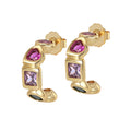 A pair of gold-colored chunky hoop earrings with vibrant purple cubic zirconia stones set in them.